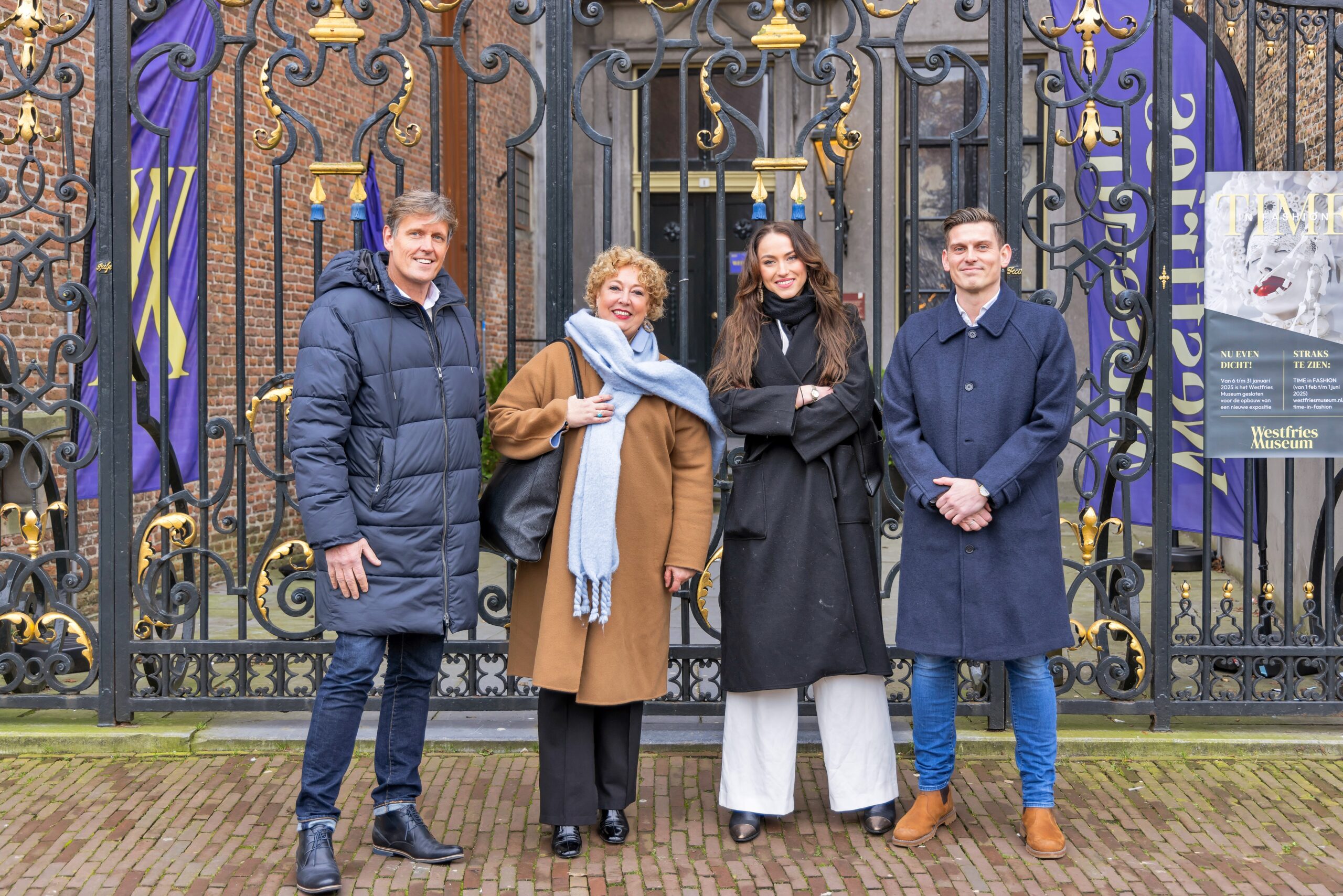 Vier medewerkers van De Stijl Makelaardij poseren lachend voor het hek van het Westfries Museum, gekleed in nette winterjassen.